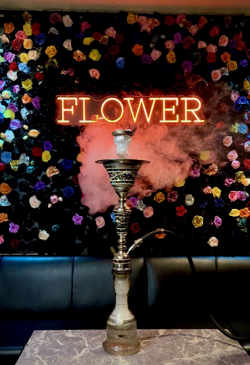 色とりどりの造花で埋め尽くされたFLOWERの花壁を背に、テーブルに置かれたシーシャ